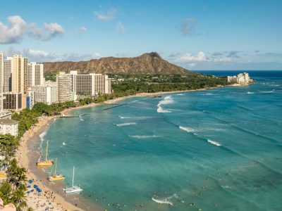 Wide view of the Waikiki coastline. Apartment buildings are on the left and the blue ocean is on the right.