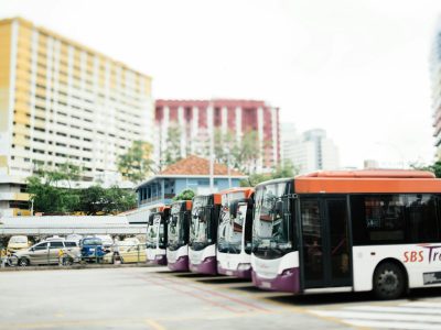 Buses lined up at a bus depot with tall buildings in the background.