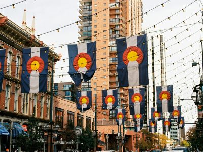 Several Colorado flags hanging from string lights over a city street.