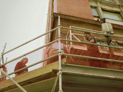 Three construction workers on scaffolding. They are working on the side of a brick building.